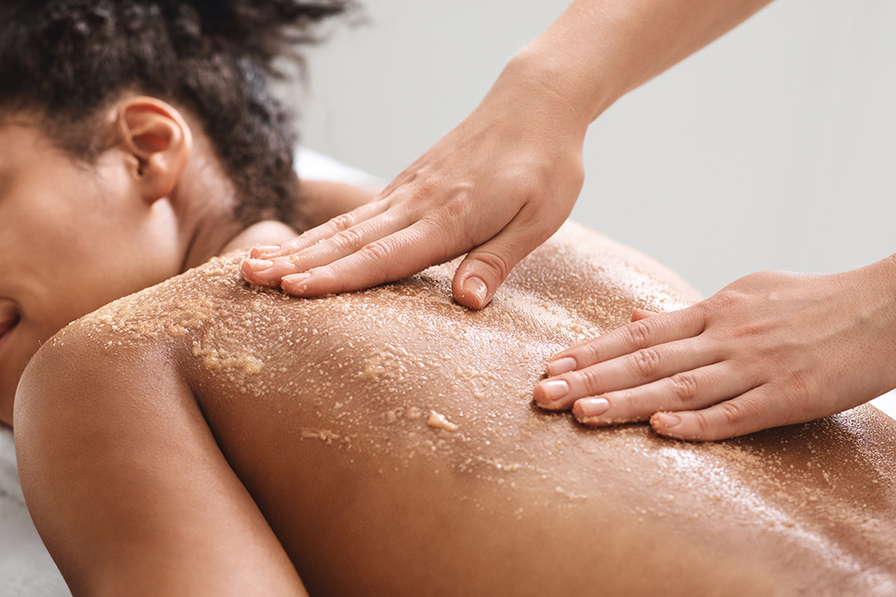 African american relaxed lady having skin scrubbing procedure at spa salon, closeup. Spa therapist applying exfoliating body mask on sleeping black woman back at luxury spa, body care concept