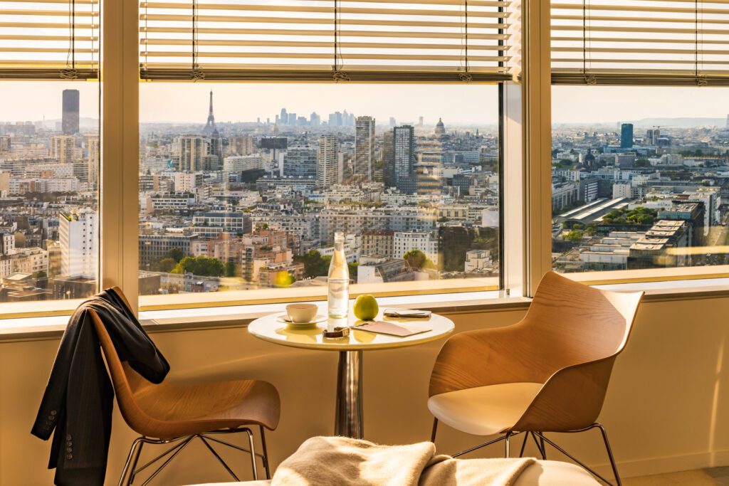 Vue panoramique sur Paris et la Tour Eiffel depuis une chambre du TOO Hôtel, avec un coin détente baigné de lumière.