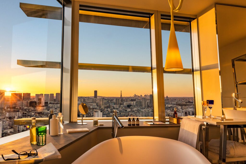 Salle de bain avec baignoire et vue panoramique sur Paris et la Tour Eiffel au coucher du soleil depuis le TOO Hôtel.